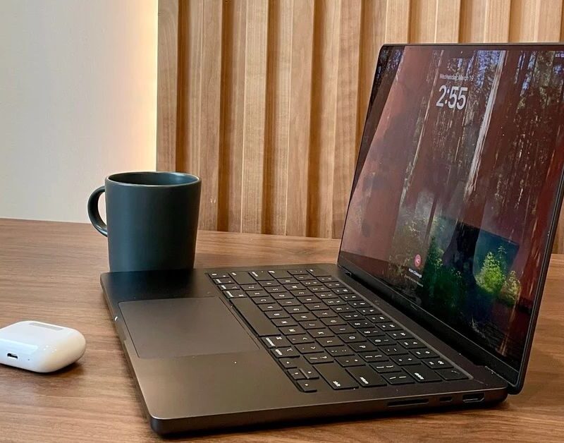 close up of a laptop and a coffee mug and a pair of wireless headphones on one of our open coworking spaces at Brick & Mortar