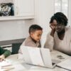 Parent working from home at a kitchen table with children, illustrating the challenge of separating work and home life.