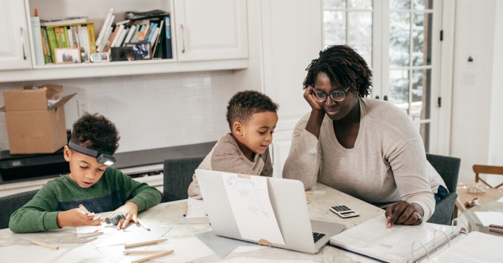 Parent working from home at a kitchen table with children, illustrating the challenge of separating work and home life.
