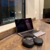 Laptop and headphones on a wooden desk by a window, offering a change of setting for a work from home routine.