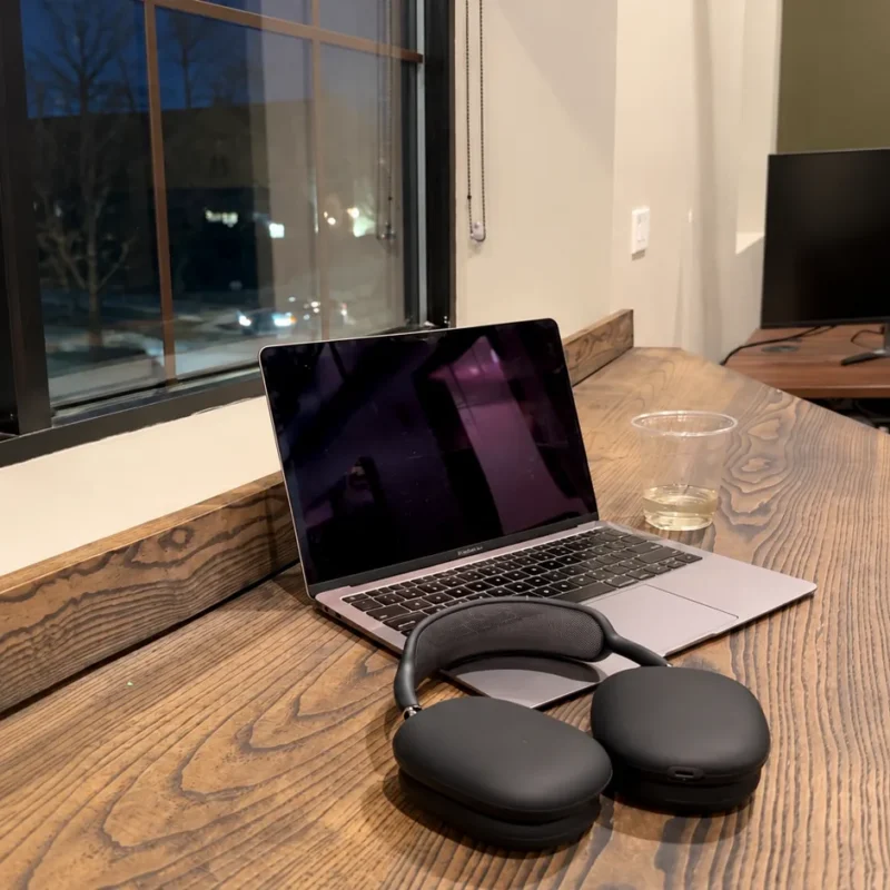 Laptop and headphones on a wooden desk by a window, offering a change of setting for a work from home routine.